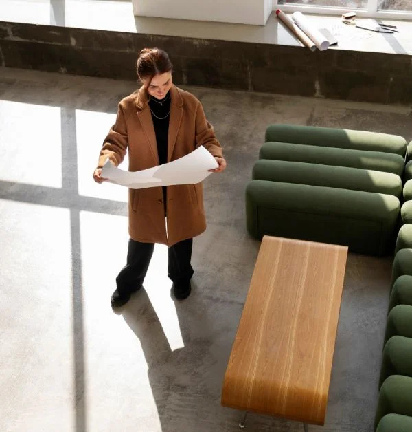 Professional interior designer reviewing architectural floor plans in a modern industrial office with green modular seating.