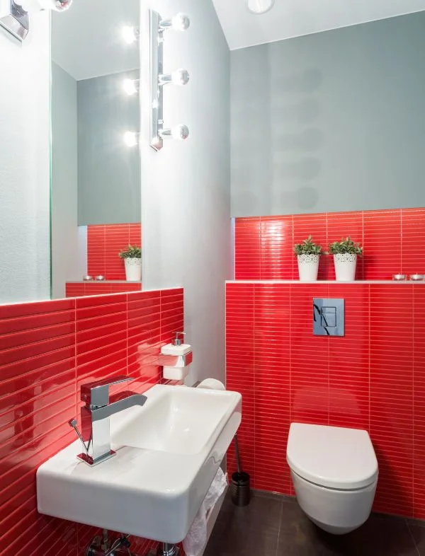 Modern bathroom featuring vibrant red glossy kit-kat wall tiles, a white wall-mounted sink with chrome faucet, and a sleek wall-hung toilet.