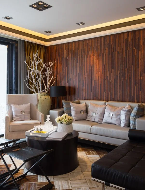 Modern living room featuring a vertical wood slat accent wall, a light grey leather sofa with silk pillows, and a black drum coffee table on a parquet wood floor.