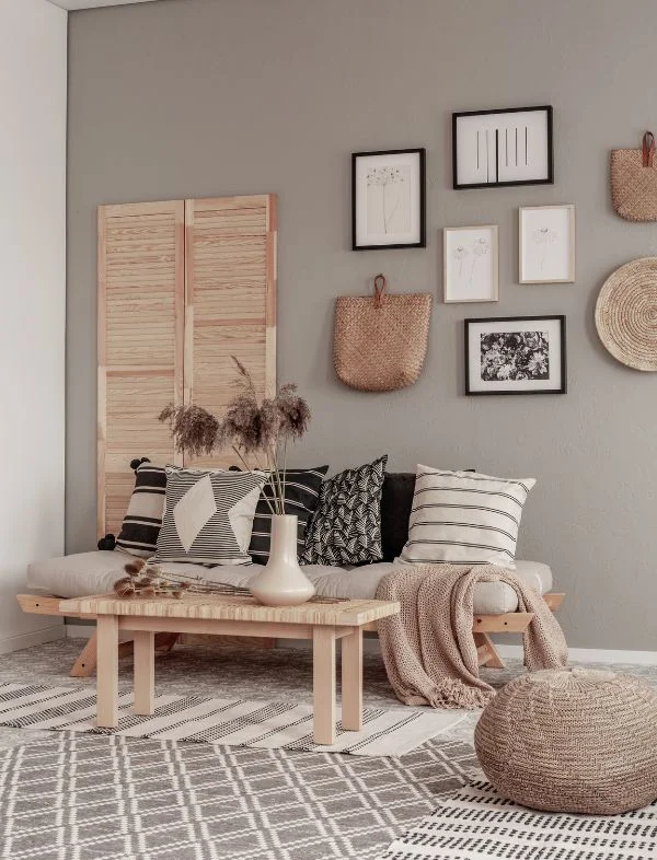 Scandi-Boho living room featuring a wooden futon-style daybed with black and white patterned pillows, a neutral gallery wall with botanical art, and woven seagrass wall hangings.