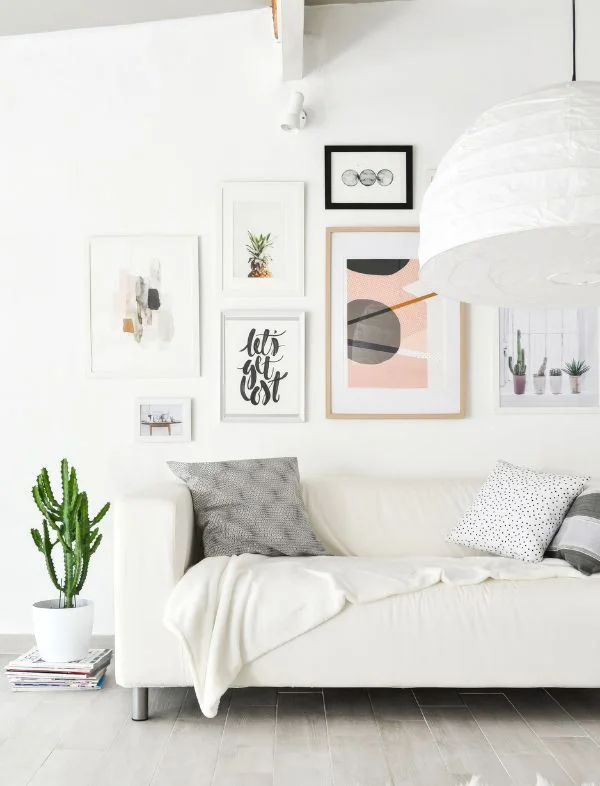 Modern minimalist living room featuring a white sofa with patterned throw pillows, a curated gallery wall with abstract art prints, and a large white paper globe pendant light.