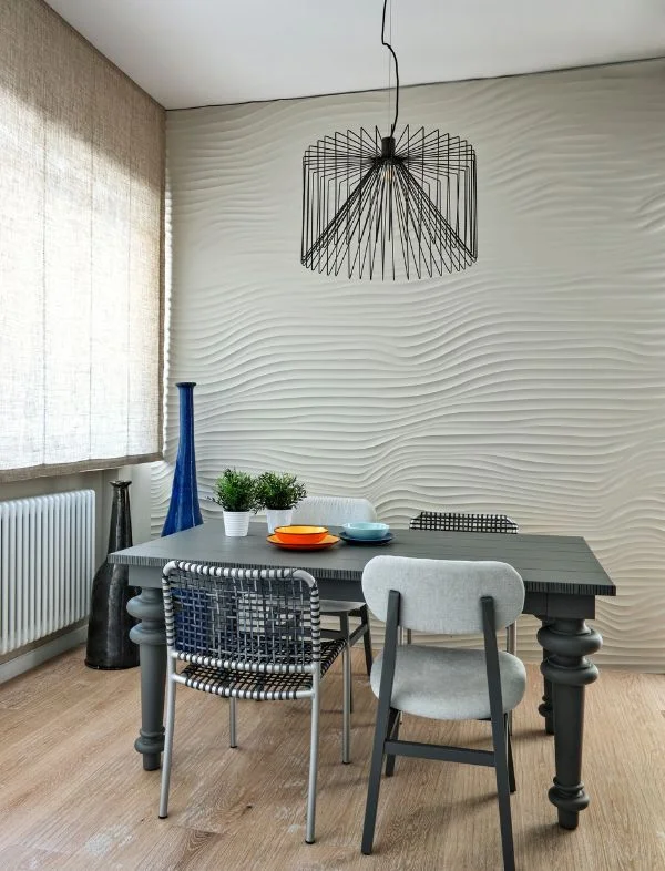 Modern dining room featuring a 3D wave-textured feature wall, a black wire cage pendant light, a dark grey dining table, and a mix of woven and upholstered mid-century chairs.